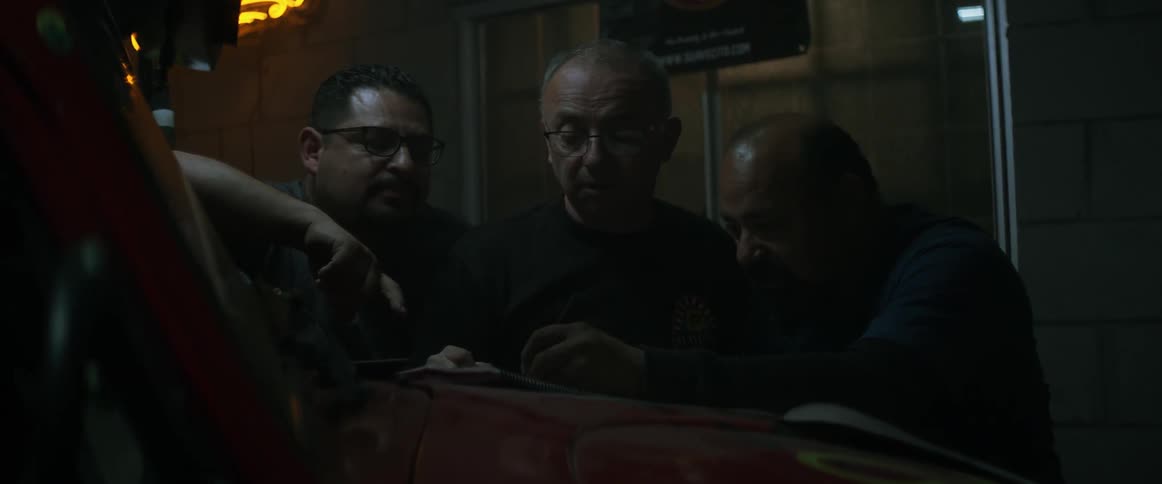 Men work on a car and converse in a garage