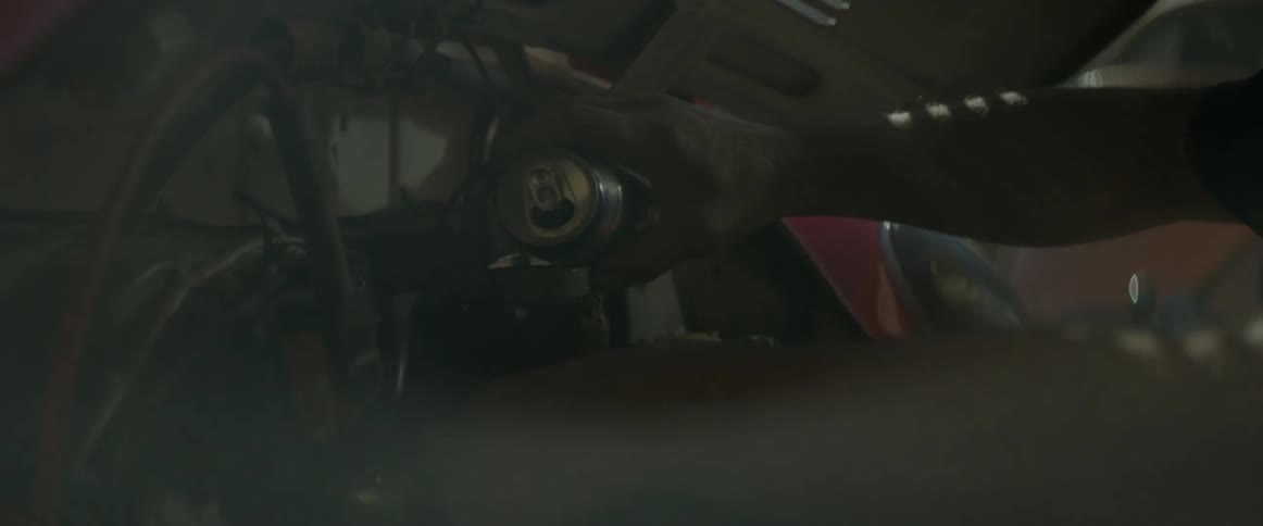 A man pours a canned drink into an auto engine then sips from the drink