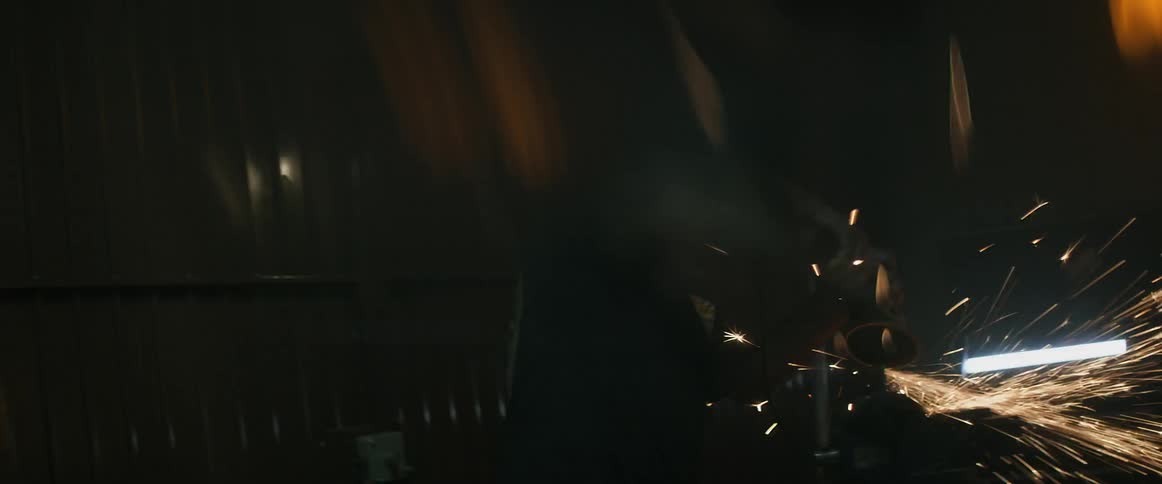 A man grinds an auto part in a garage casting off sparks into the air