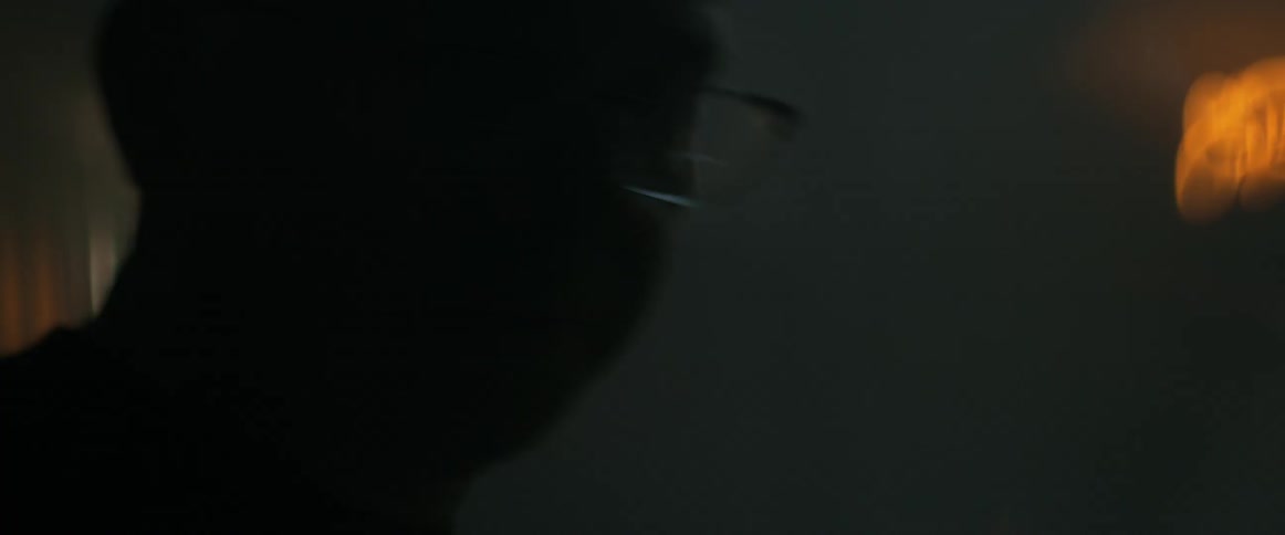 A man stands next to a neon light in a dark room
