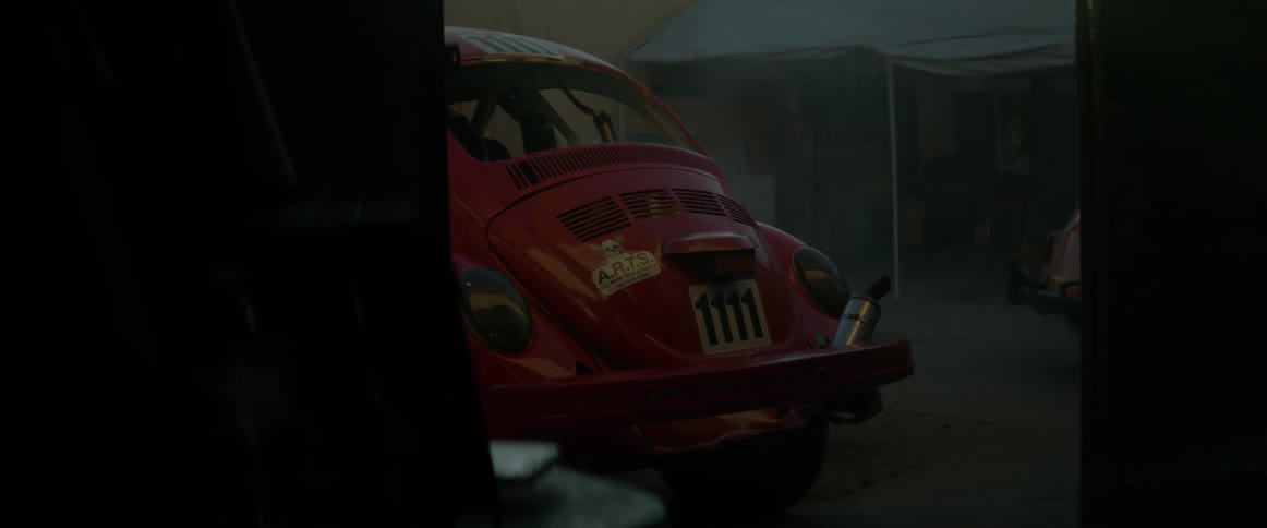 A car painted with race numbers sits in a lot outside a garage