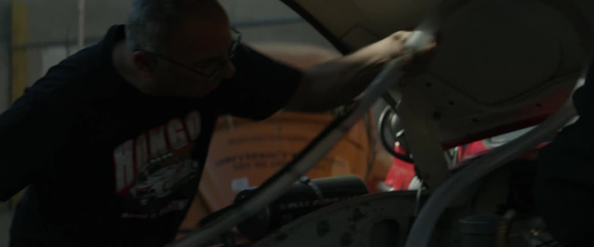 A man adjusts a hose attached under the hood of a car