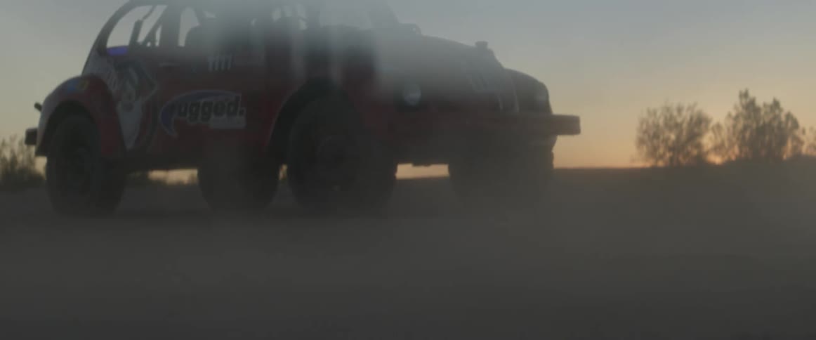 Dirt drifts across the ground from the wind in front of a rally car