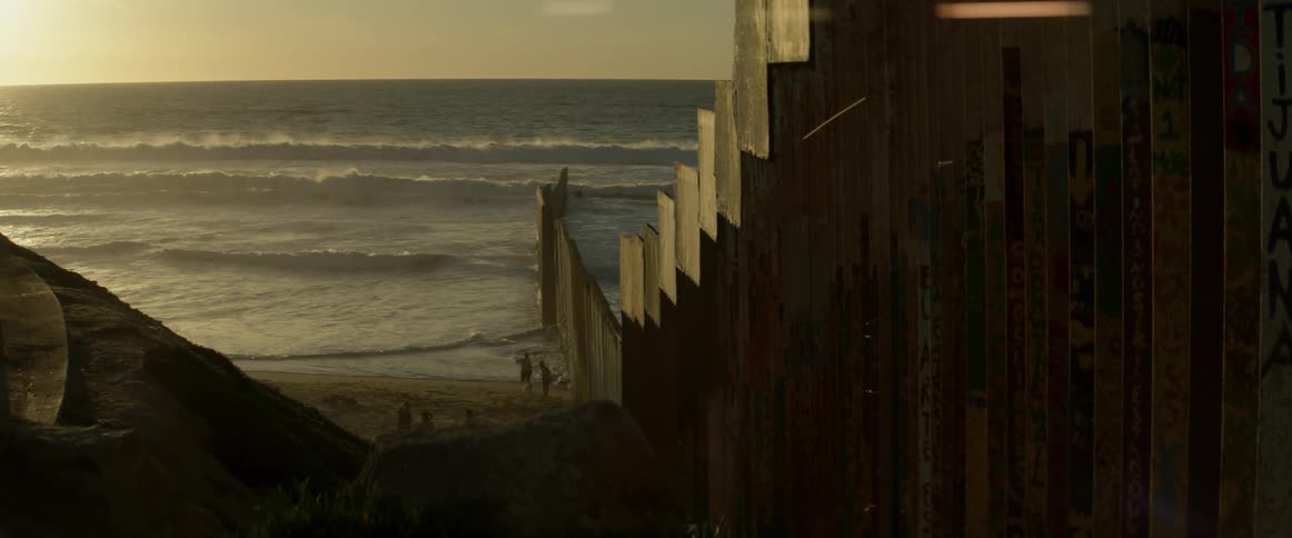 Couple walking on a beach in the distance beyond a wall