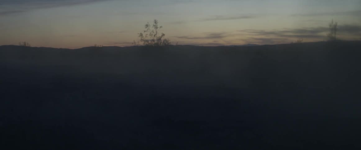 Dust blows across a desert landscape at dusk