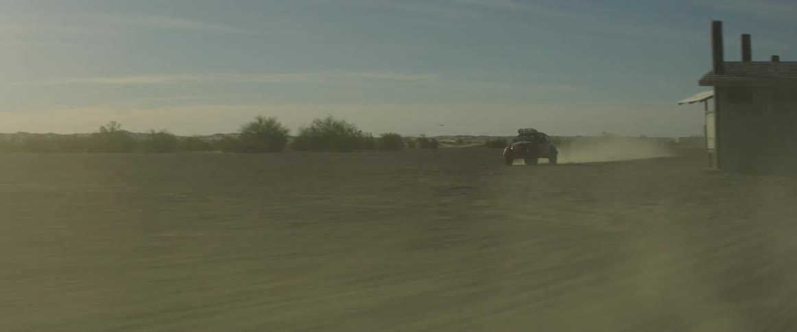 A car leaves a dust trail as it races over sand in the desert
