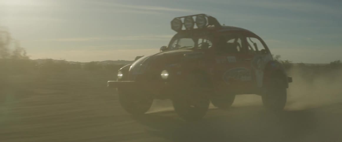 A vw bug bounces and kicks up dust as it races in an off-road race