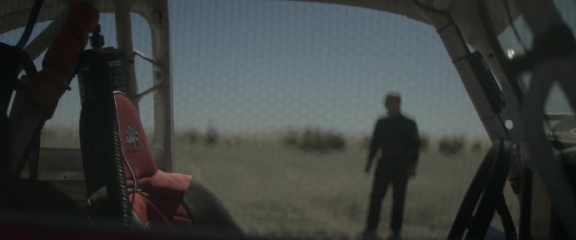 A man is standing in the desert by a vehicle