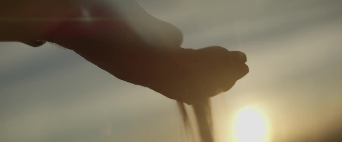 A person holds out a hand full of sand and sifts it through their fingers