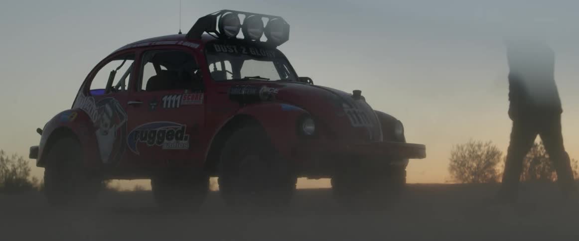 A race driver gets into a vw bug as dust blows around it