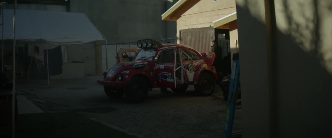 A man walks around an off-road race car he is working on