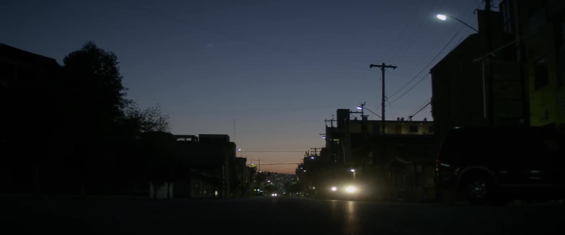 Cars with their headlights on travel down the street at night