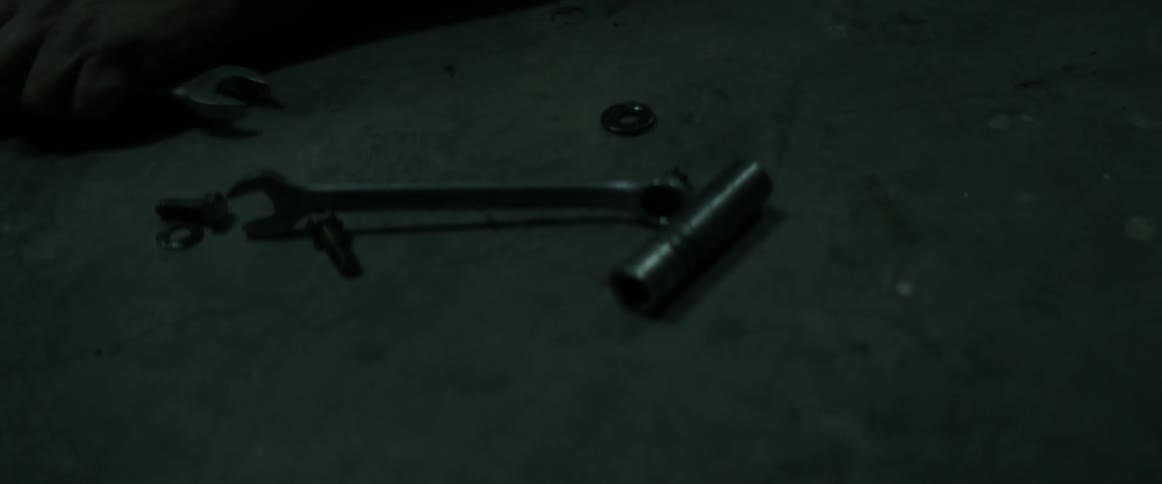 Wrenches sit on the ground as a man works on a car