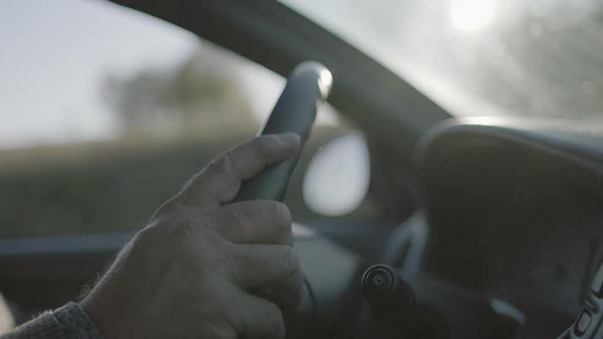 A man's hand holds onto a steering wheel while he drives on a sunny day