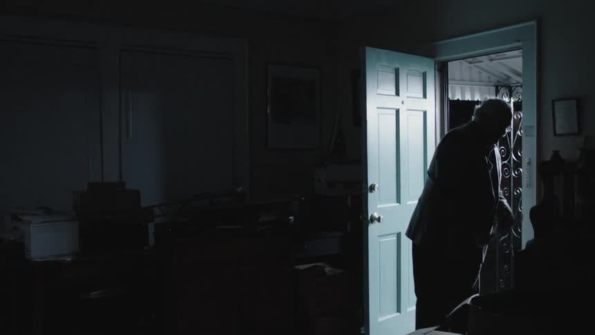 A man enters a dark house and takes off his hat