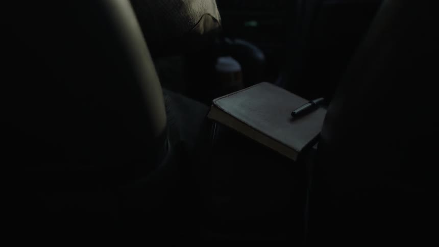 A person drives a car with a notebook sitting on the center console