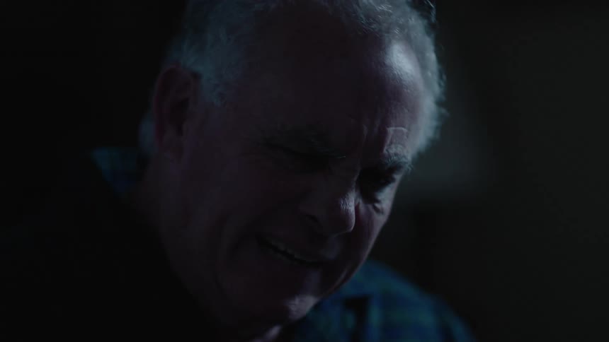 A man with gray hair rubs his face and yawns