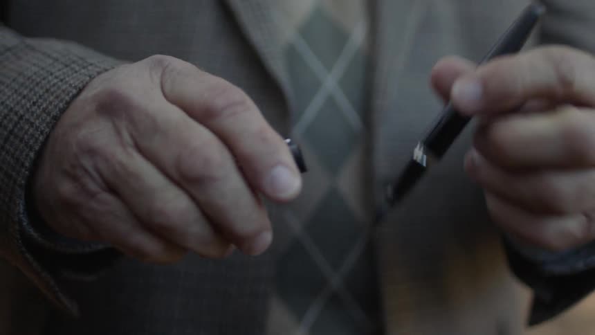 Man wiping a pen before closing it and putting in an inside jacket pocket