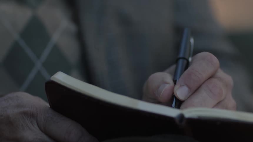 A man writes in a notebook with a pen
