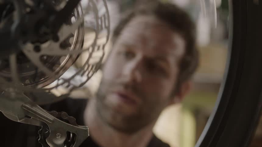 A man is working on a bicycle's wheel and gears in a bike shop