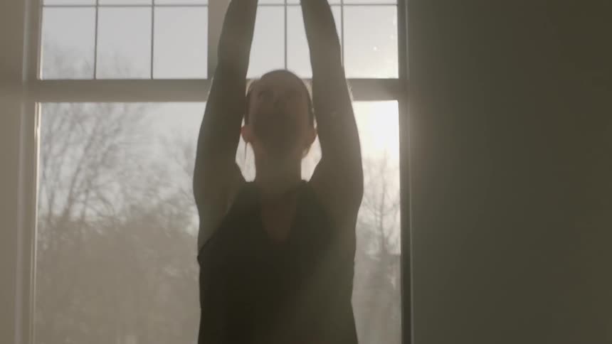 A woman does yoga poses in front of a sunny window