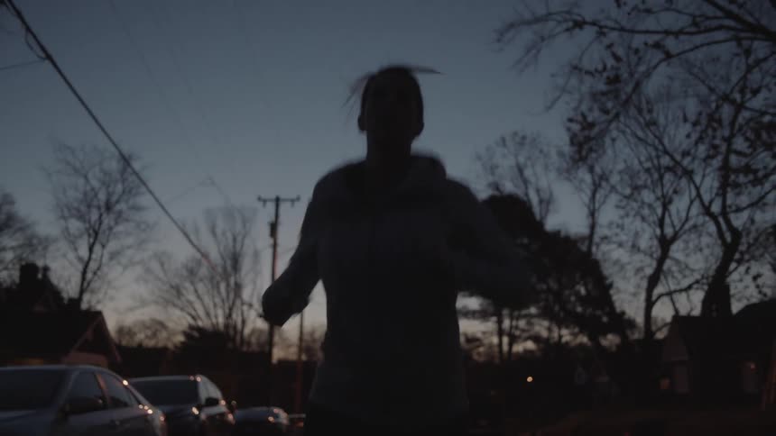 A woman jogs on a residential street at dusk