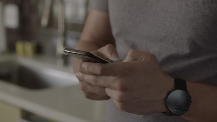 A man typing on his cell phone while leaning against a kitchen cabinet