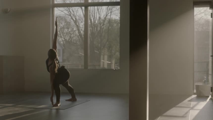 A woman does yoga poses inside a sunny room
