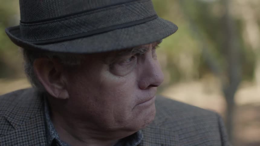 An older man is sitting outside thinking and nodding his head