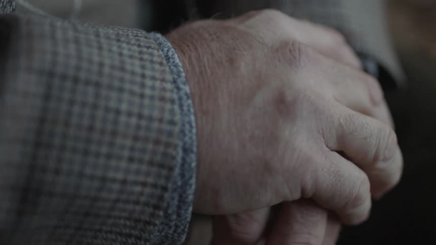 An elderly man tries to steady his shaking hand