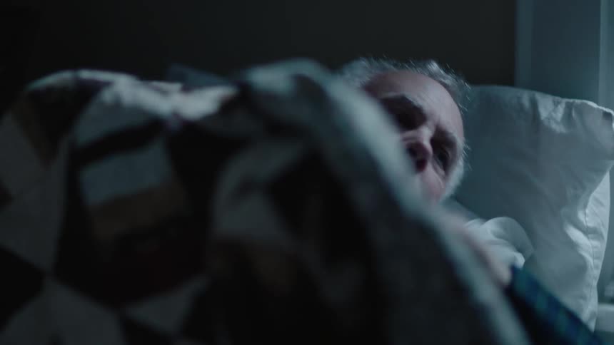 A sleeping man wakes up and sits up in bed
