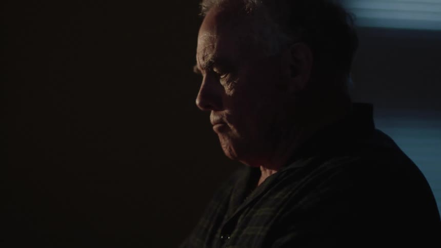An older man sits down at a desk to write