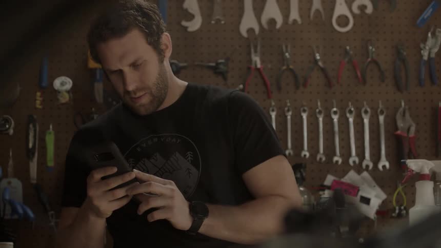 A man is checking his cellphone while he stands in a bike shop