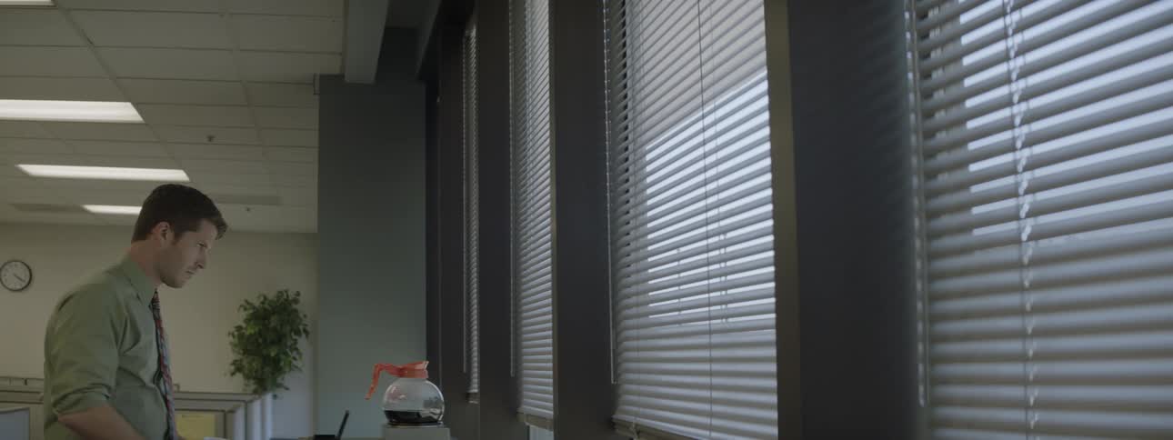 A man in an office pours himself a cup of coffee then looks outside