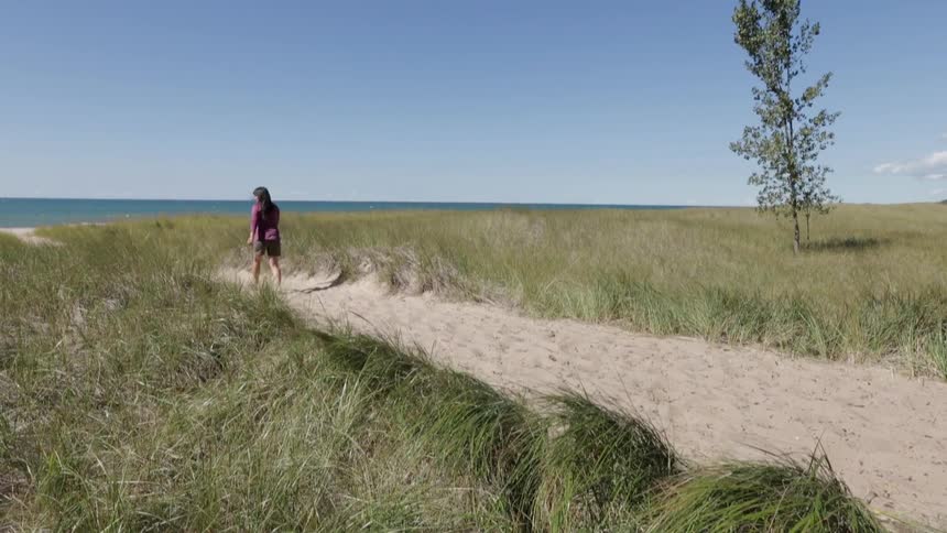 A woman walks towards the ocean on a clear day