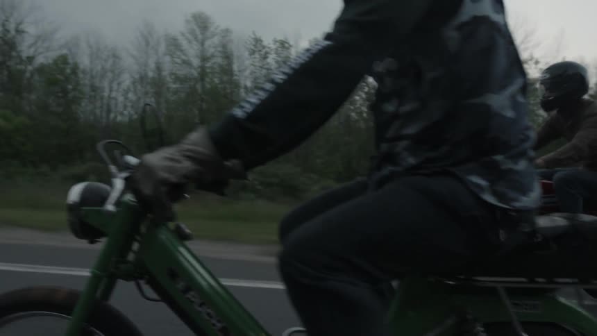 Motorcyclists ride on a rural road on a cloudy day