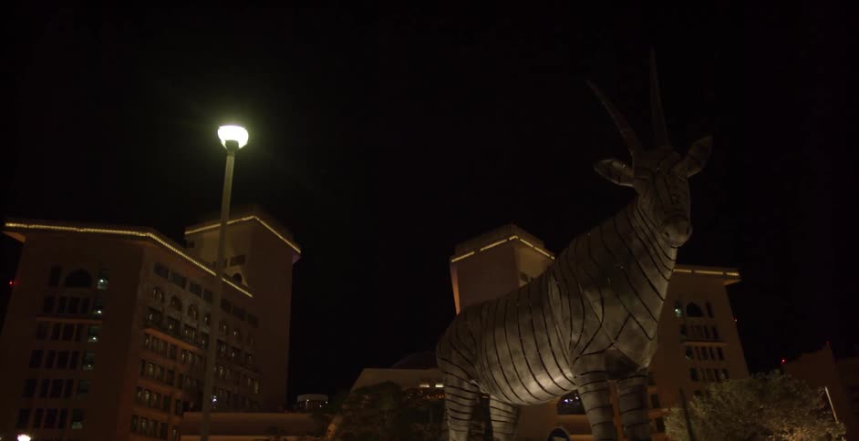 A view of a large animal statue next to some buildings at night time