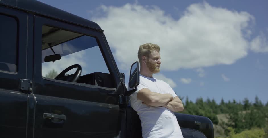 A man leans against a vehicle on a sunny and windy day