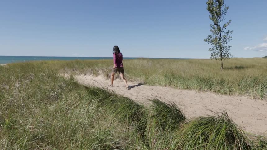 A woman walks on a sandy trail leading toward a shoreline