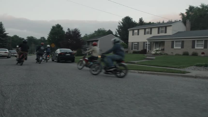 A group of people rides motorcycles through a neighborhood