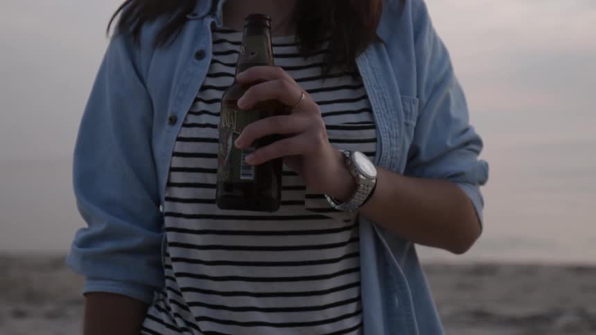 A woman holds a beer near a beach bonfire
