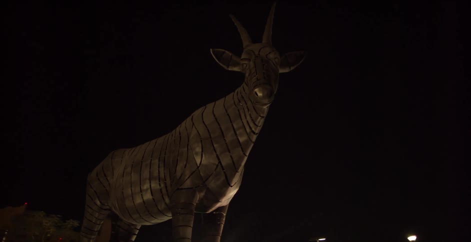 A statue of an antelope stands in a city at night