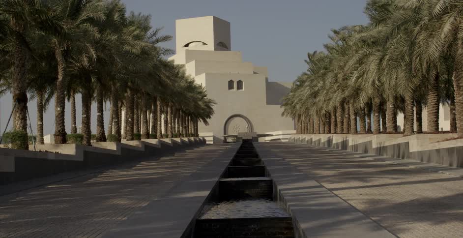 Water flows down a water feature in front of a white building and palm trees