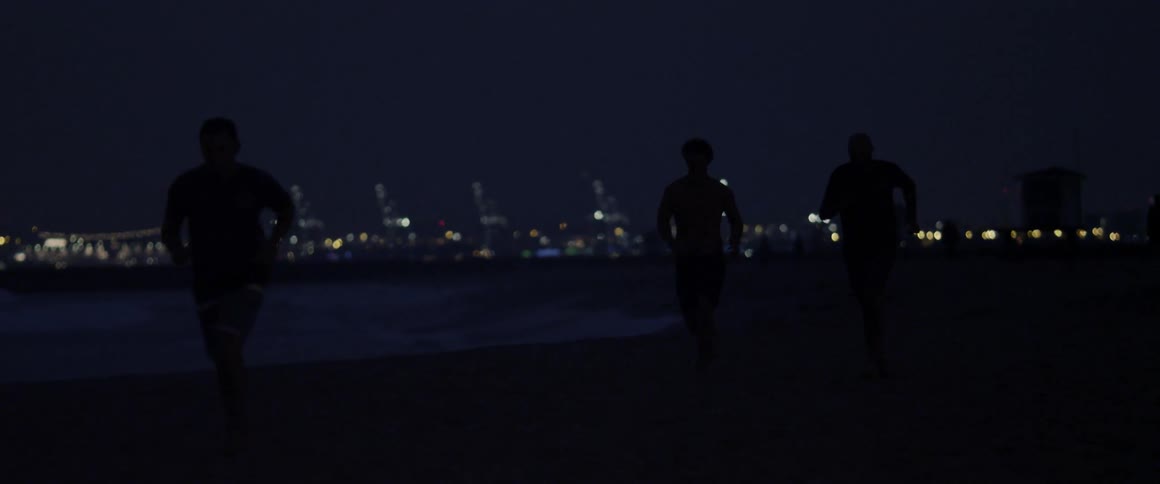A group of men jog on a beach at night
