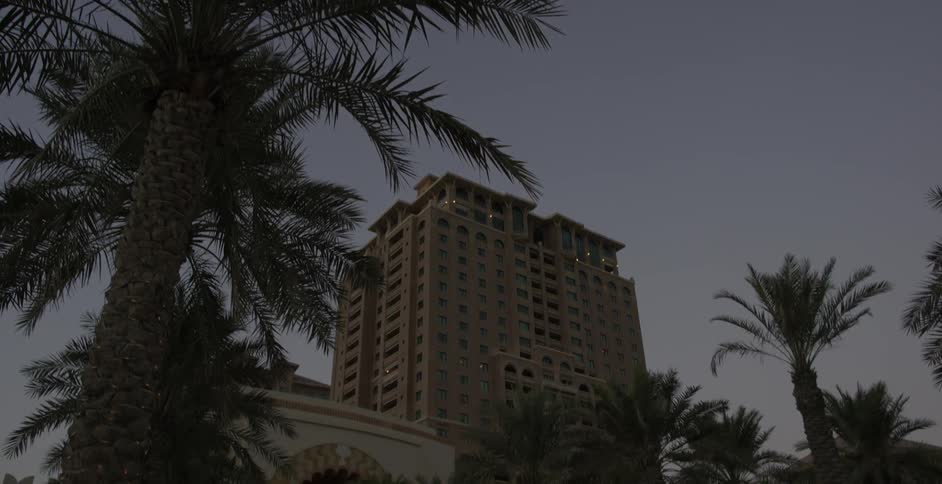 A high-rise building towers above palm trees at dusk
