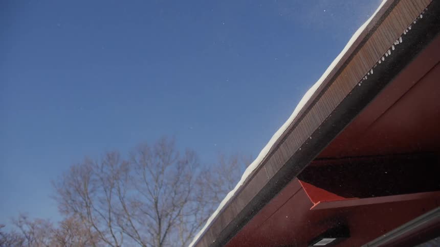 Snow drifts off a rooftop on a sunny winter day