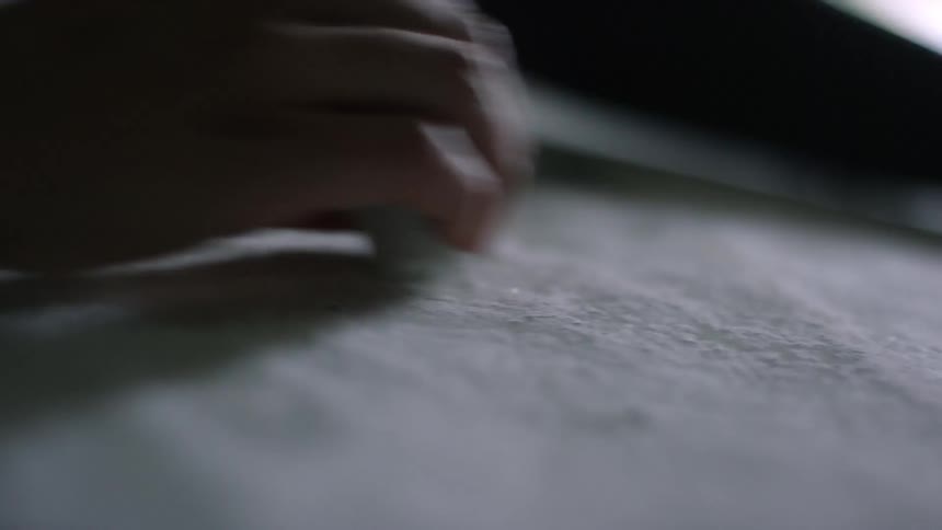 A person in a wetsuit waxes a surfboard