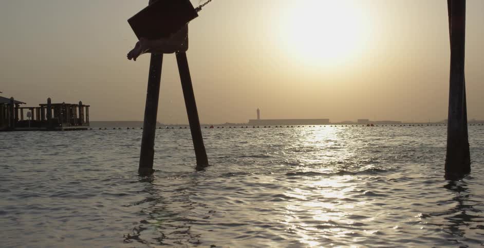 A woman swings on a beach at sunset