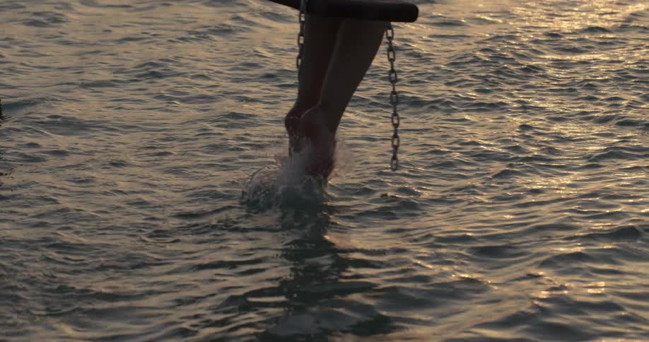 A woman's toes skim the surface of the water as she swings above it
