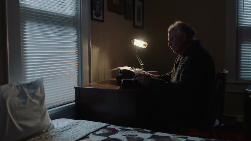 Man sits at a dimly lit desk and flips through a book